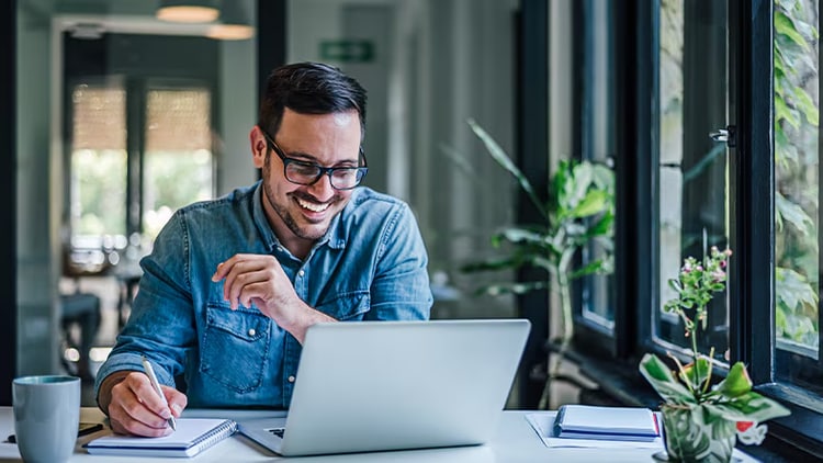 Steps to transformation: man smiling at a laptop while jotting notes