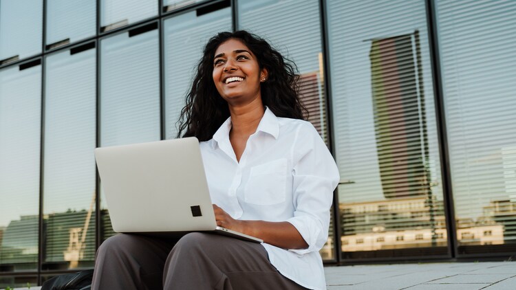 Woman sitting on the ground and smiling with an open laptop in her hands