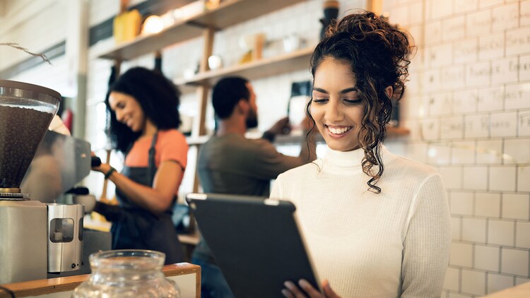 GenAI chatbots: woman smiling at a tablet behind the counter of a coffee shop, with two other workers in the background