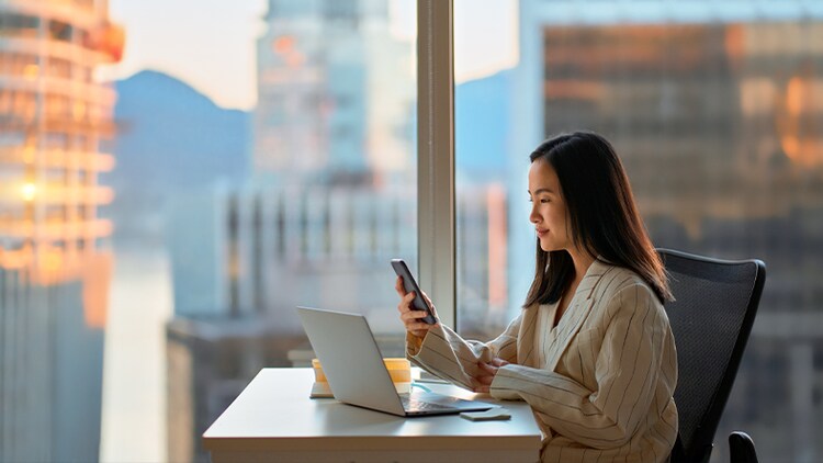 AI adoption: woman sitting at a desk in front of office window in a high-rise building looking at her phone