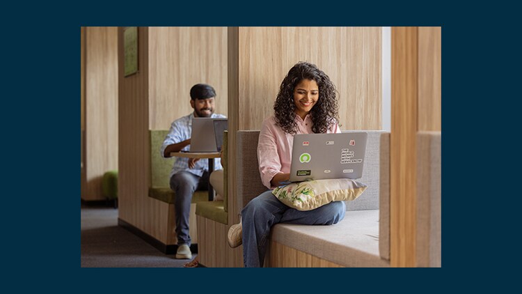 Skill kit: two employees smiling at their laptops in the ServiceNow India Technology and Business Center