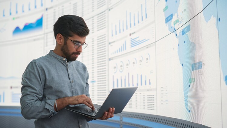 Risk in the age of AI: man holding laptop in front of graphs and charts on a large screen
