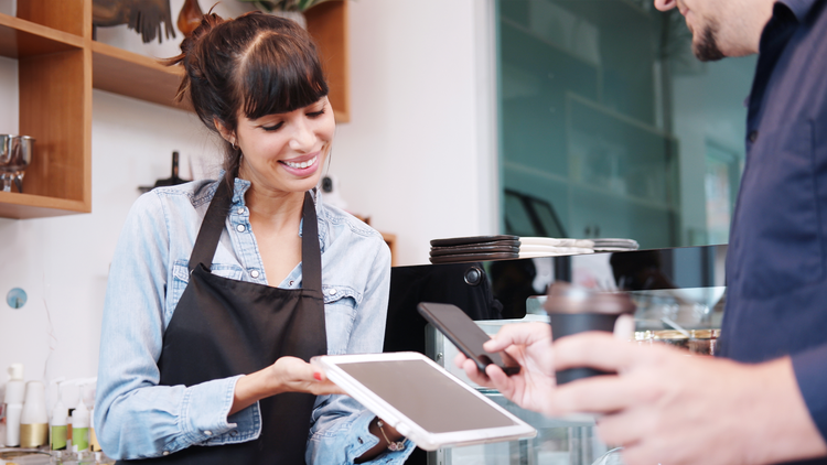 AI maturity in retail: smiling woman holding a tablet for a customer to scan with his phone