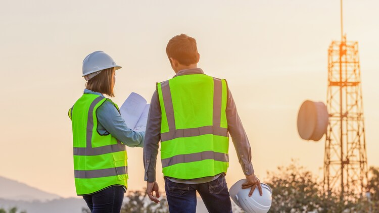 Telecom transformation: Two telecom workers in safety vests and helmets in front of a communications tower