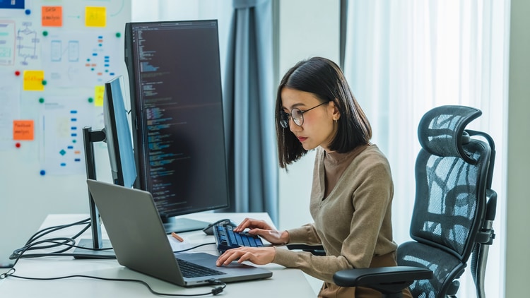 AI testing: woman typing on a laptop on a desk with computer monitors displaying code