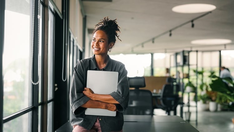 AI security: smiling woman holding a closed laptop and looking out an office window