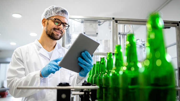 Preventive maintenance: employee at a bottling plant smiling at a tablet in his hands