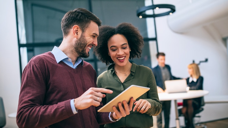 AI partnerships: two workers engaged in conversation over a tablet in a bright office