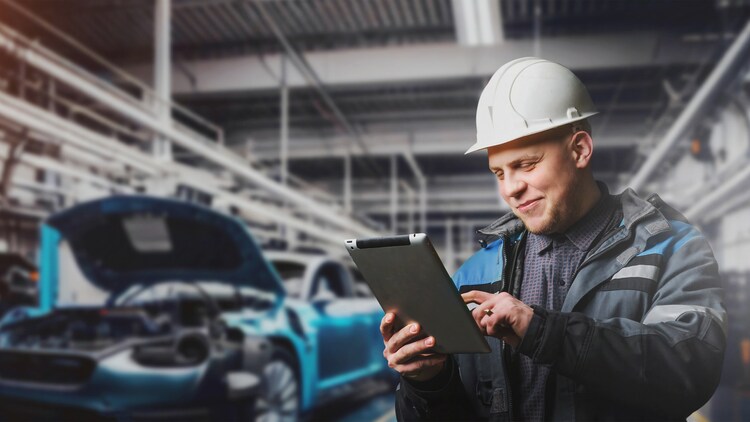 AI in the automotive industry: an automotive worker wearing a hard hat and smiling at a tablet in his hands