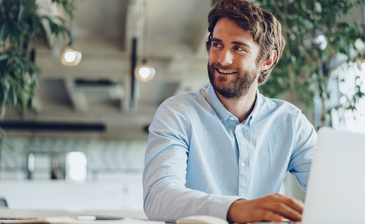 Man sitting at a desk working on a laptop and looking up and to the side