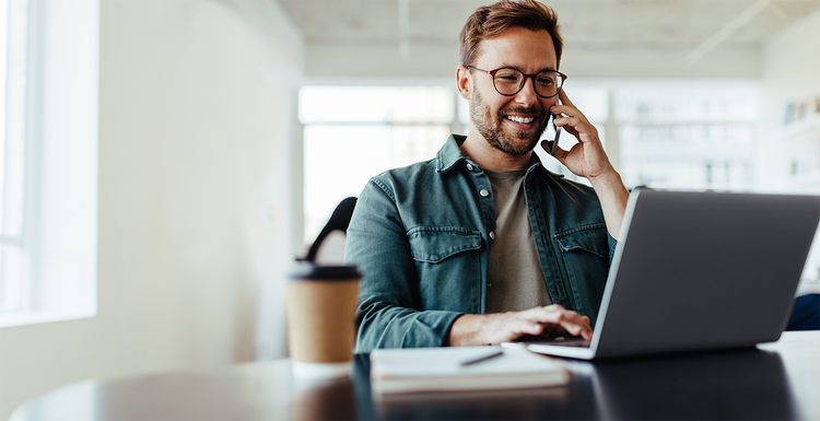 Man with a phone to his ear and his other hand on laptop