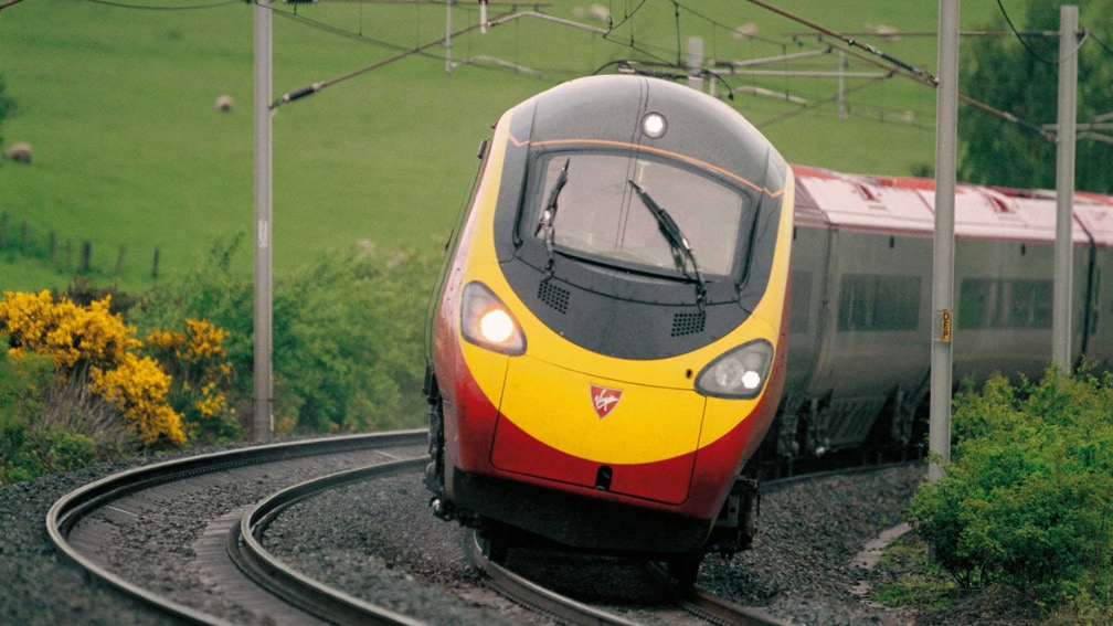 A Virgin Trains train is rounding a curve in the countryside