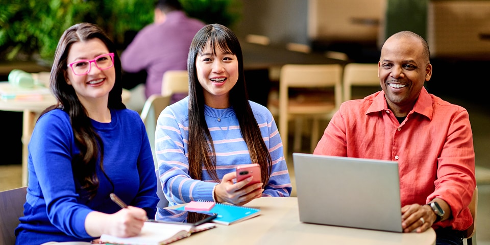Trois collègues sourient alors qu’ils travaillent ensemble autour d’une table avec un ordinateur portable et un téléphone, pour suivre une formation ServiceNow.