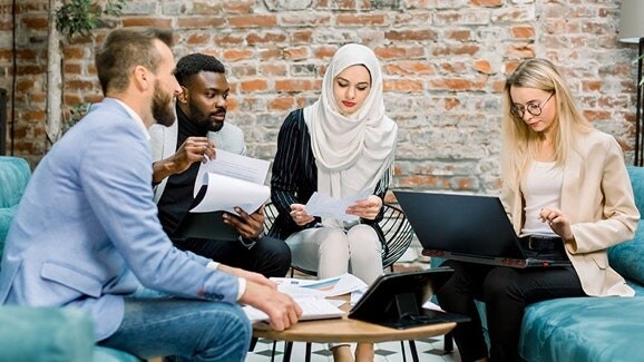 Zugehörigkeit schaffen: Mitarbeiter unterschiedlicher Herkunft arbeiten auf Sofas zusammen.