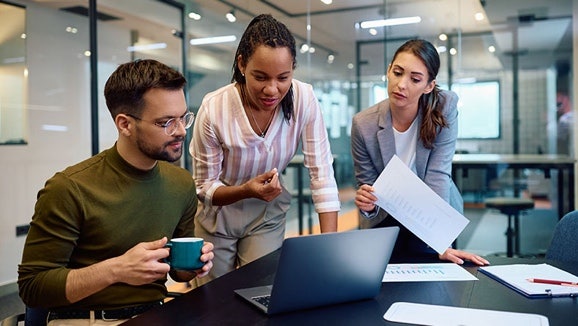Drei Kollegen arbeiten im Büro an einem Laptop zusammen