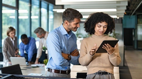 Zwei Geschäftsleute, die in einem modernen Büro über ein Tablet zusammenarbeiten