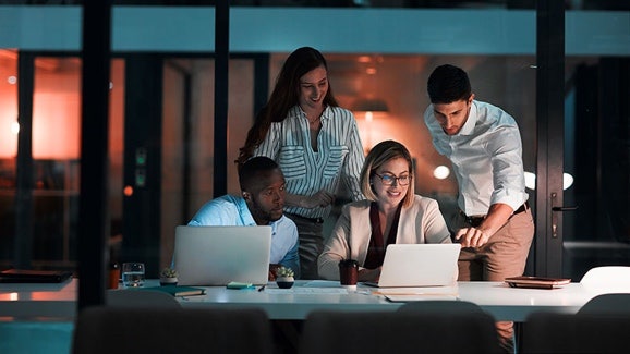 Eine Gruppe von Menschen, die spätabends in einem Büro arbeiten, konzentriert auf ihre Laptops