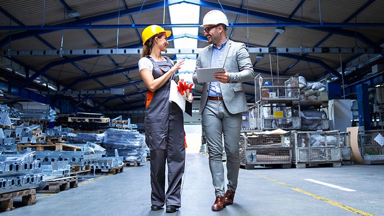 Deux travailleurs du secteur industriel avec des casques de sécurité marchant dans un entrepôt