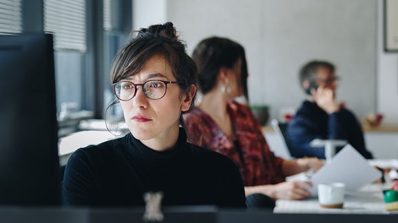 Portrait d'une femme d'affaires travaillant sur un ordinateur dans un bureau avec des collègues en arrière-plan
