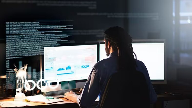 IA générative et développement low-code : homme de dos, assis devant un moniteur à double écran affichant un tableau de bord