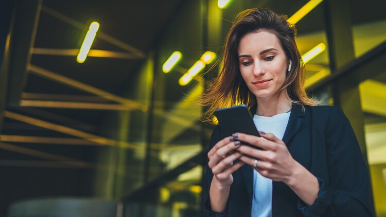 L’automatisation collaborative : une femme debout devant une fenêtre reflétant des lumières jaunes, avec un téléphone dans les mains
