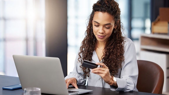 IA dans les services financiers : femme tenant une carte de crédit dans une main et tapant sur un ordinateur portable de l’autre main