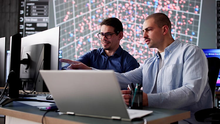 Two colleagues in cyber data team monitoring computer technology in office