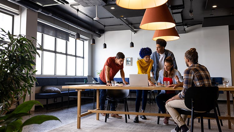 Un groupe de collègues collaborant autour d'un ordinateur portable dans un espace de travail moderne et lumineux