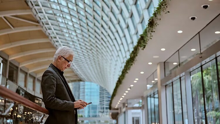 Hybrid work wayfinding technology: man standing in office building looking at phone in his hand