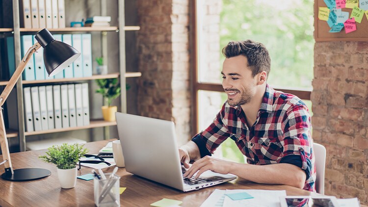 AI aan het werk zetten voor mensen in verschillende branches: een werknemer kijkt op kantoor glimlachend naar zijn laptop