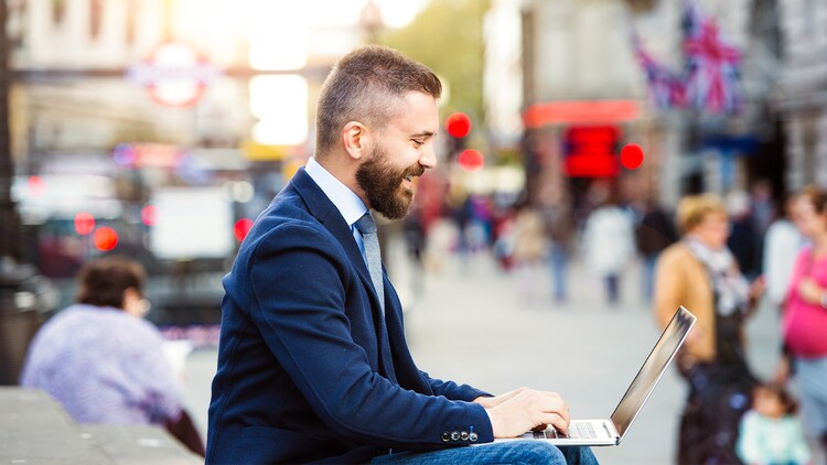 Gegevenssoevereiniteit: een man die buiten in een drukke omgeving in Londen lacht terwijl hij op zijn laptop werkt