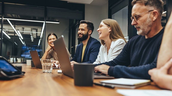 Een groep professionals in een modern kantoor, die vergaderen en glimlachen terwijl ze laptops gebruiken