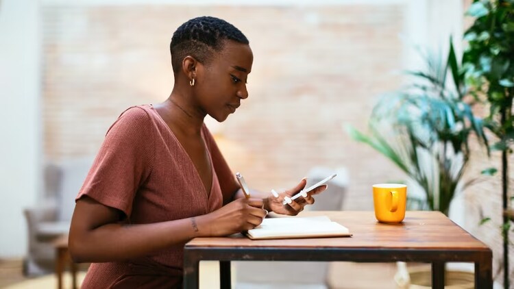 Women at a desk and looking at phone and writing notes.