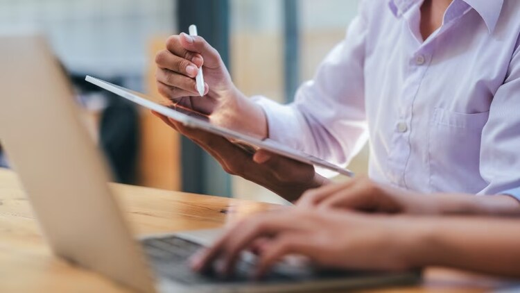 Close up of typing on a laptop and writing on a tablet.
