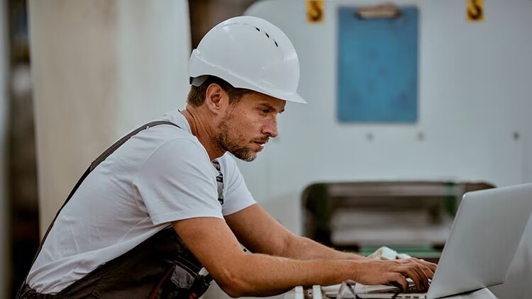 Cybersecurity in manufacturing: worker in a hard hat typing on a laptop