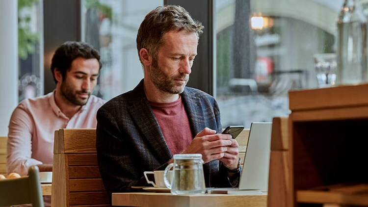 Connected ecosystem: man in a coffee shop looking at a smartphone in front of an open laptop