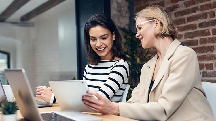 Digital experiences: 2 women looking at a tablet in front of open laptops