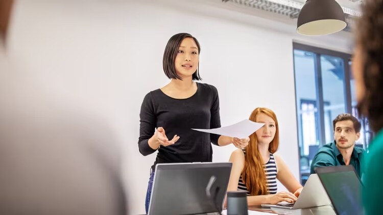 AI in knowledge management: Woman leading discussion in a conference room while workers look on