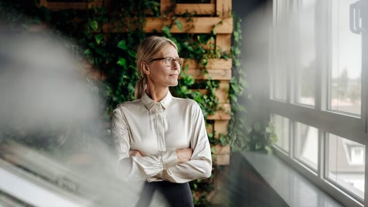 ESG reporting: businesswoman standing against an ivy-laced background looking out a window