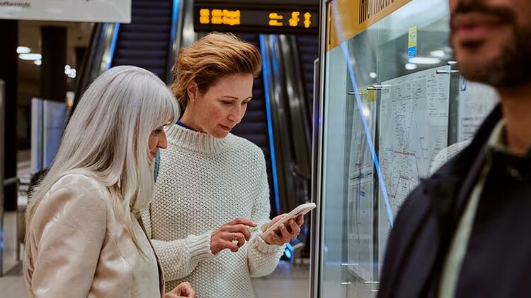 AI-powered customer experience: two ladies looking at a smartphone at a transit stop