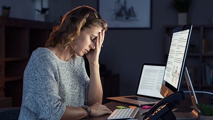 Employee burnout: overworked woman in front of a computer with her face in her hand and eyes closed