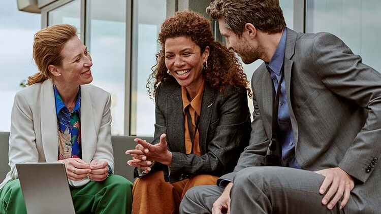 Total experience for long-term success: 3 co-workers seated, smiling with a laptop
