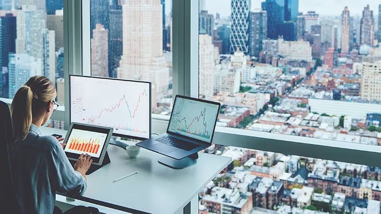 Banking cyber risk: woman viewing graphs on computer screens in high-rise office