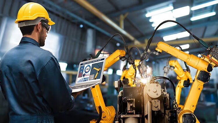 Manufacturing innovation: worker in hard hat looks at open laptop in front of robotic technology