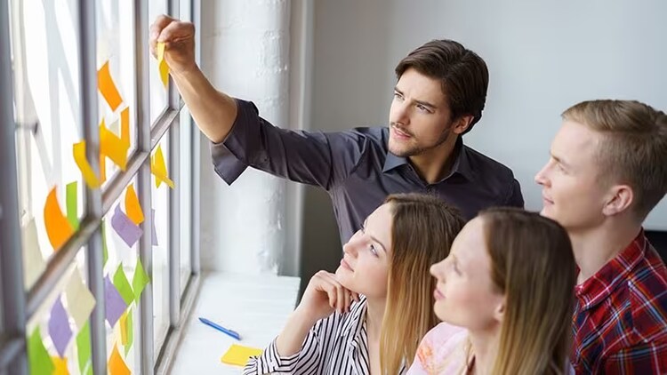 Innovative companies: 4 workers looking at sticky notes on a window