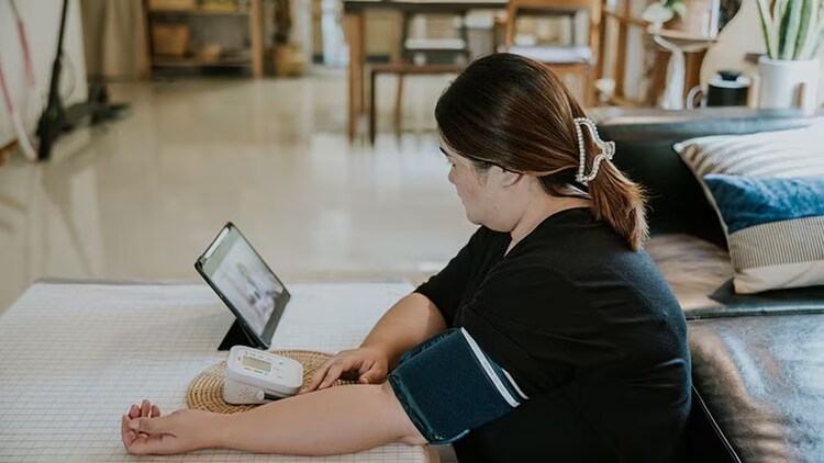 Virtual wards: Female with blood pressure cuff in home environment looking at tablet screen