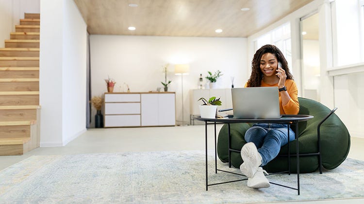 Employee satisfaction: woman working on her laptop and talking on the phone in a bright, modern living room
