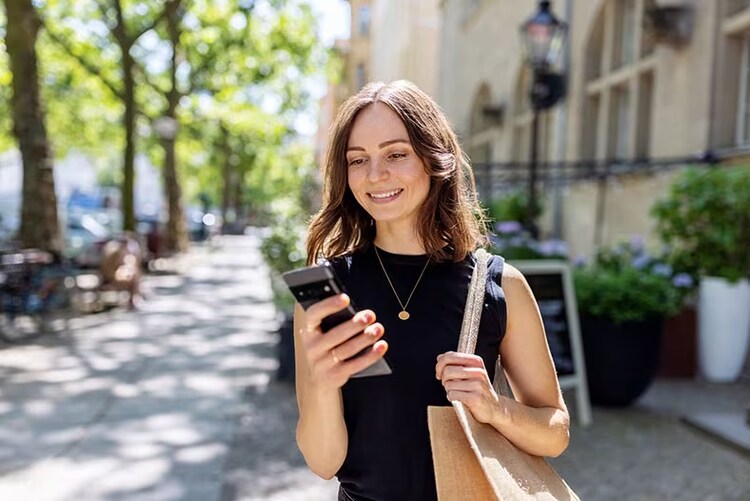 Customer experience predictions: smiling woman outdoors looking at smartphone in hand