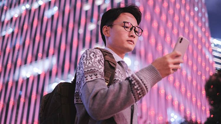 Ways to use generative AI: Asian man looking at smartphone against pink-lit tall building