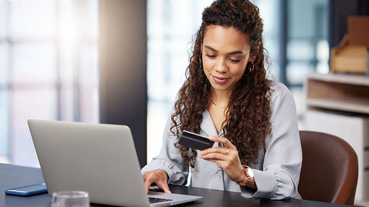 AI in financial services: woman holding a credit card in one hand while typing on a laptop with the other
